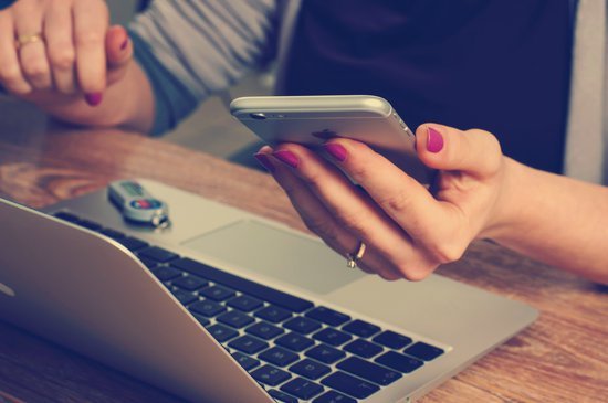 person at computer looking at their phone